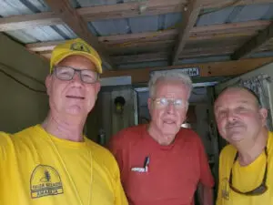 Two Alabama Baptist Disaster Relief volunteers in yellow shirts stand on either side of a man they served in South Carolina.